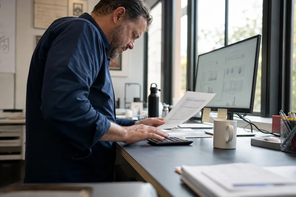 Agency owner checking a monthly software budget on a printed spreadsheet with a calculator